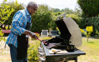 An elderly man cleans an outdoor barbeque